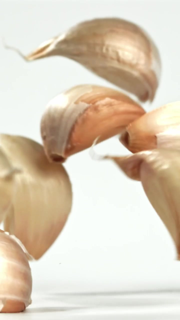 Spicchi d'aglio che cadono al rallentatore su sfondo bianco