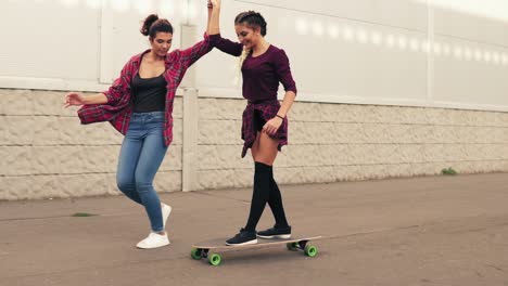 Laughing-young-hipster-girl-being-taught-skateboarding-by-a-friend-who-is-supporting-her-holding-her-hand.-Slow-Motion-shot
