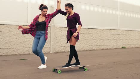 laughing young hipster girl being taught skateboarding by a friend who is supporting her holding her hand. slow motion shot