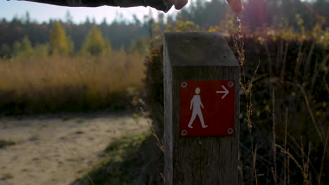 close up: man pointing at a pedestrian walking route sign in a forest