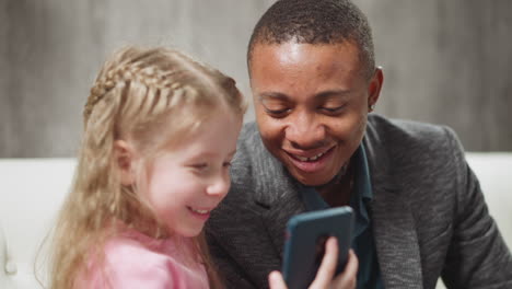 Little-girl-and-happy-African-American-man-look-at-photos