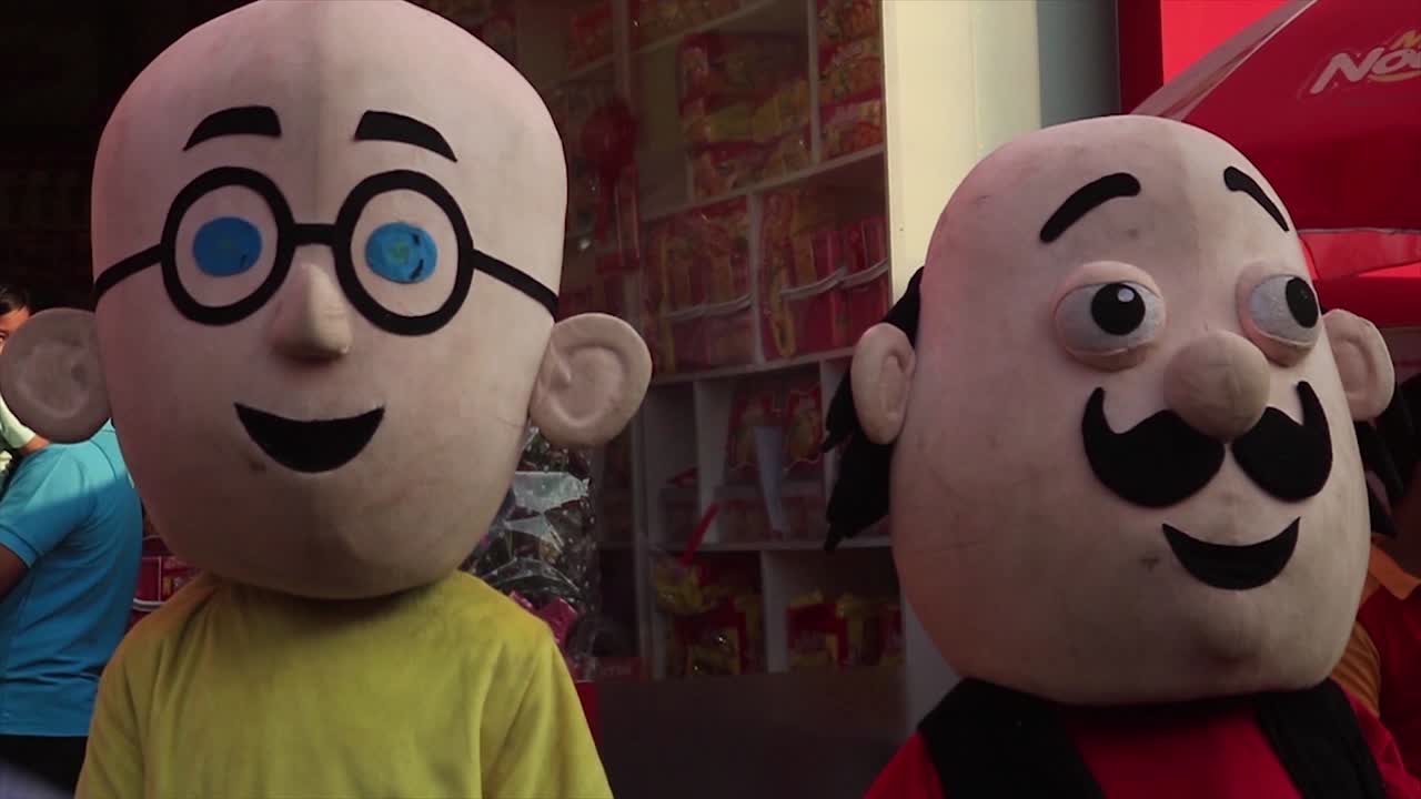 Two people wearing Motu and Patlu costumes at a Bangladesh market