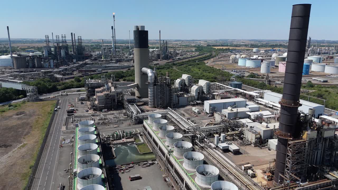 Wide aerial drone view of industrial power plant infrastructure, including turbines, smoke stacks, and cooling systems producing electricity in UK