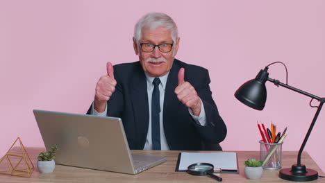 Senior-business-man-raises-thumbs-up,-agrees,-approve,-likes-good-news-using-laptop-at-pink-office