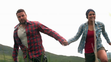 una pareja corriendo de la mano por el campo.