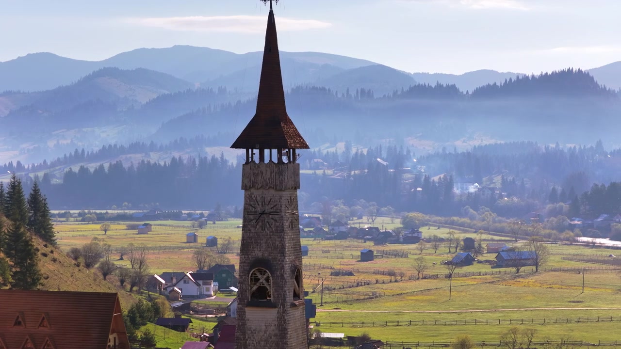 Dronebillede af et højt trækirkespir, der rejser sig over en naturskøn dal i Bucovina, Rumænien