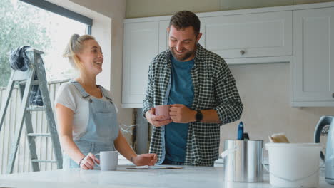 Pareja-Renovando-La-Cocina-En-Casa-Mirando-Muestras-De-Pintura-En-Una-Pausa-Para-El-Café