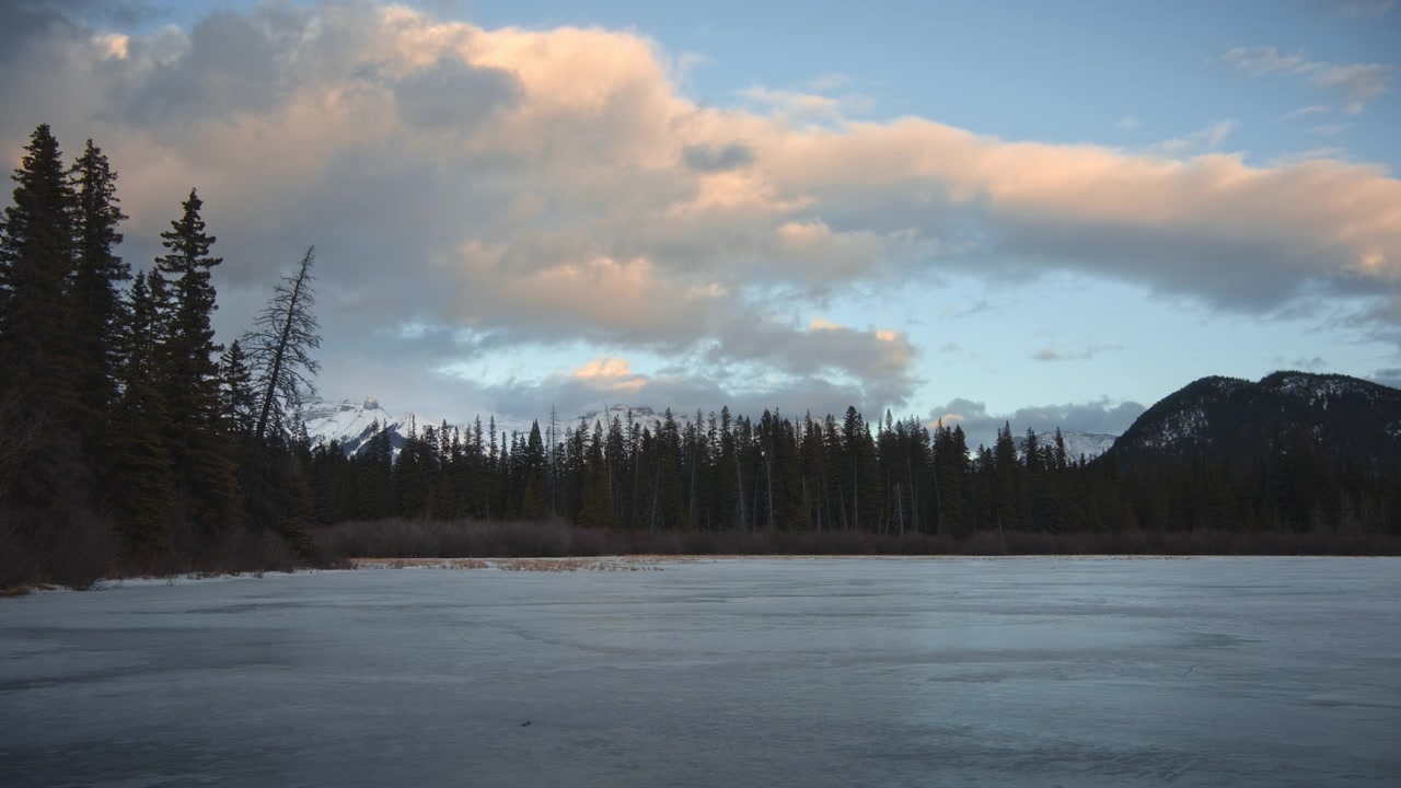 Clouds moving above frozen lake at sunset. Time Lapse