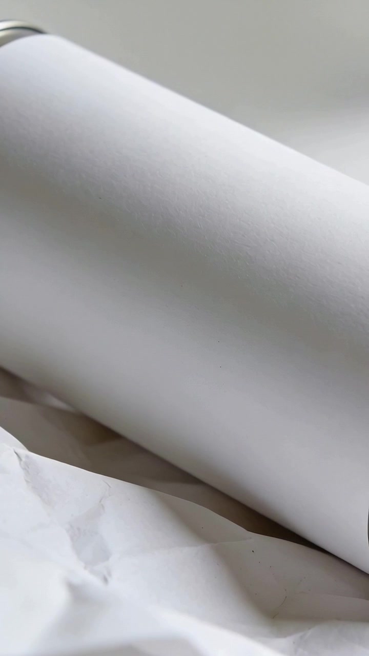 Vertical video: Camera filming tumbler lying diagonal on paper in studio with silver rim for mockup