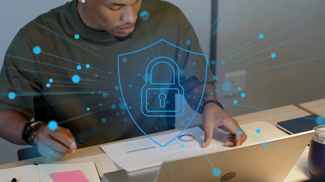 Man writing notes, particles forming shield-and-padlock over laptop, reviewing chart to secure data