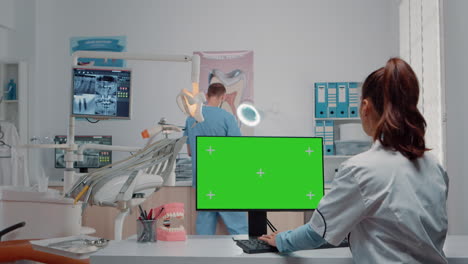 dentista usando la pantalla verde en el monitor y hablando con el asistente del hombre