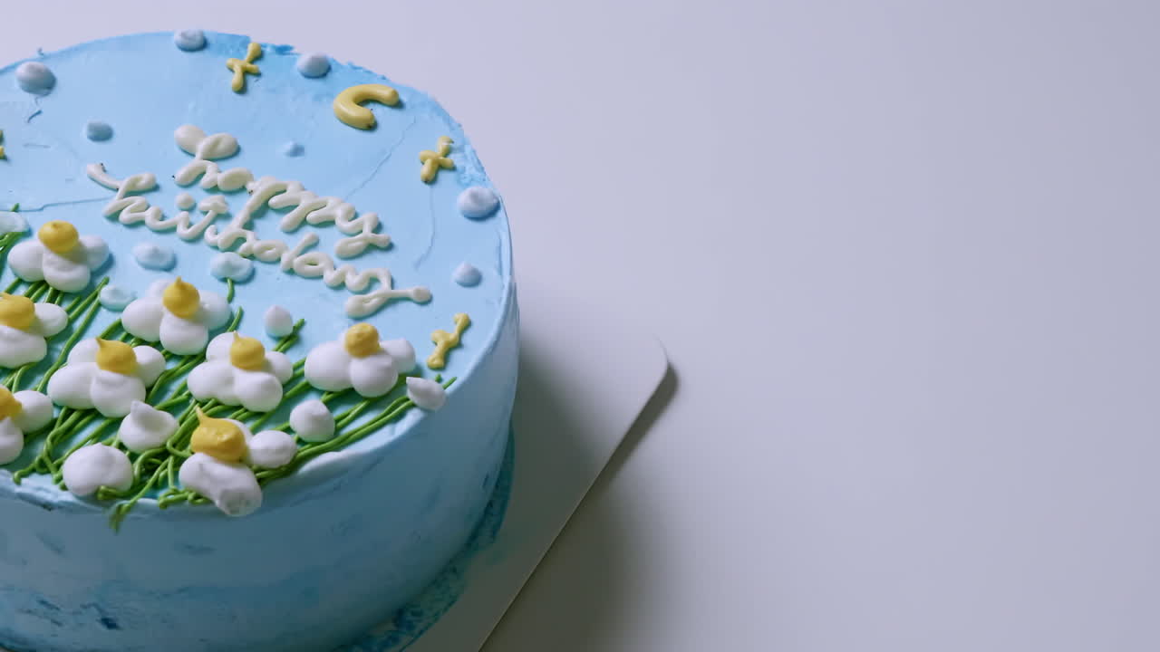 primer plano de la parte superior de un pastel de cumpleaños con glaseado azul y decorado con flores blancas y amarillas, con felicitaciones de cumpleaños en la parte superior