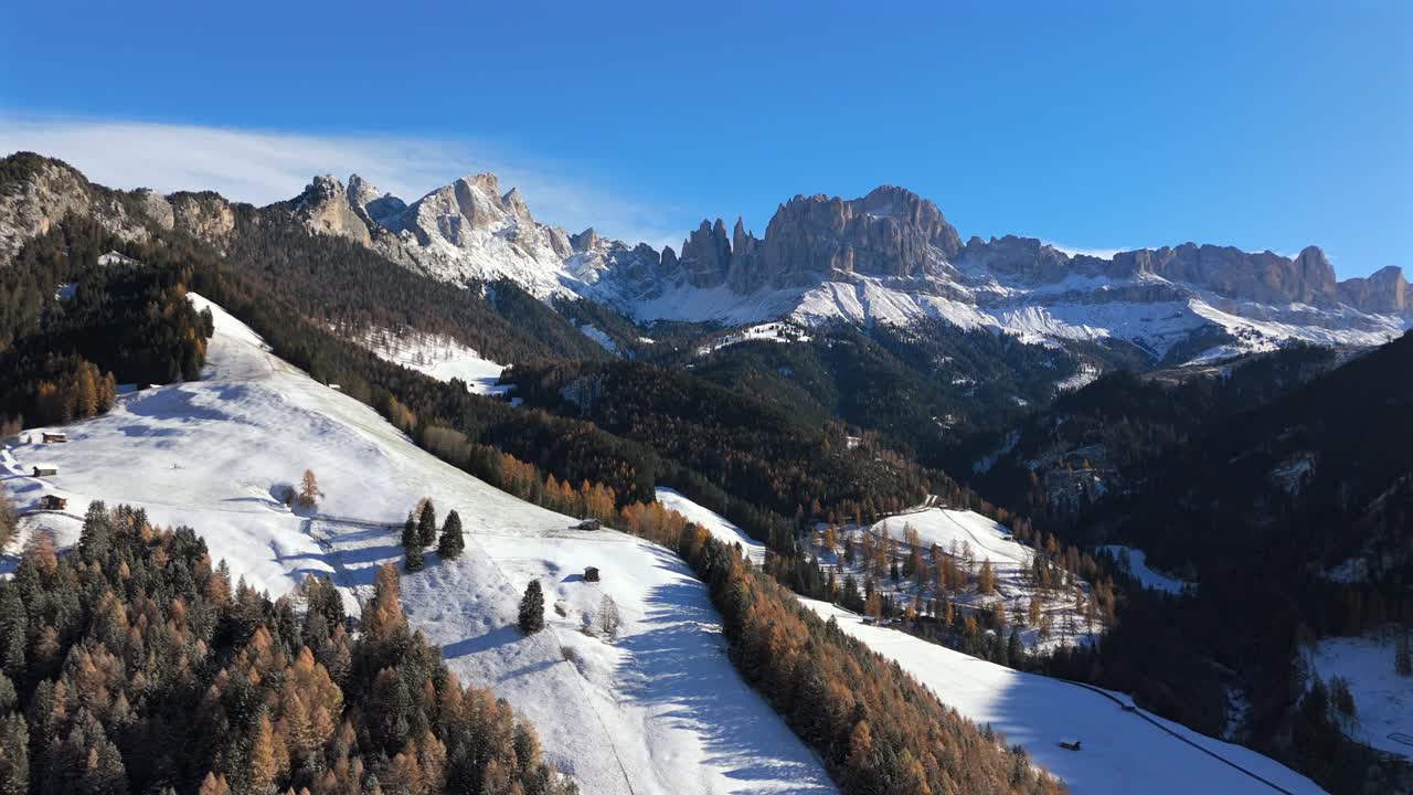 Beautiful 4K shot of snowy alpine terrain in South Tyrol, Italy, with golden forests and the dramatic Rosengarten mountain range of the Dolomites captured in bright winter daylight