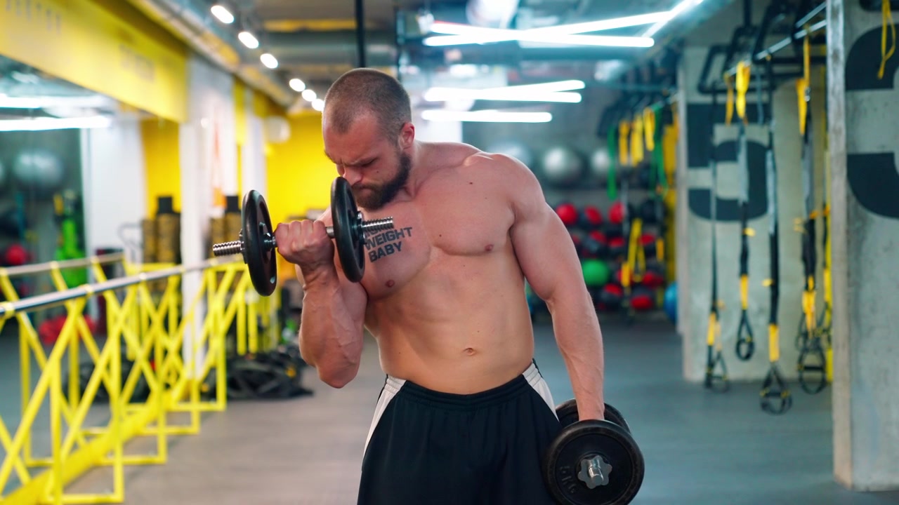Uomo muscoloso che esegue curl bicipiti con manubri in una palestra moderna