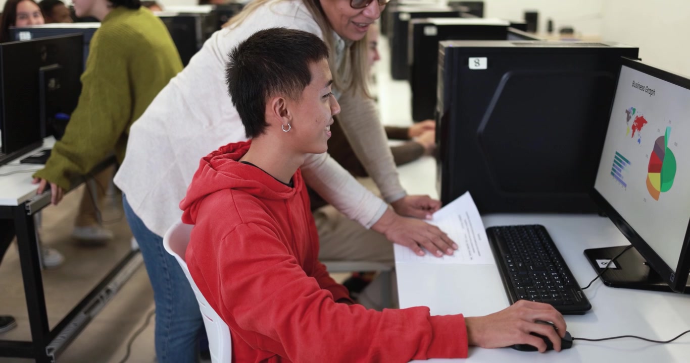 Teacher Assisting Student with Data Analysis on Computer in Classroom