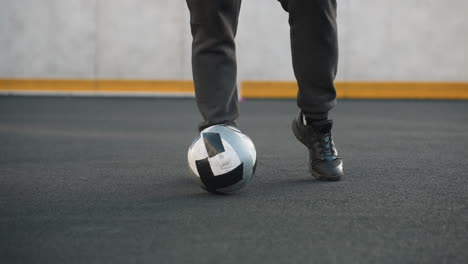 vista de la pierna de un atleta que demuestra giros precisos del tobillo con las piernas izquierda y derecha, equilibrando hábilmente la pelota de fútbol en una arena deportiva con poste de portería y pared pintada