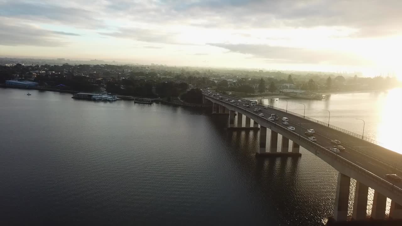 Aerea: Ripresa con drone che segue auto che attraversano un ponte verso la città durante l'ora di punta mattutina, mentre il sole sorge a Sydney, Australia.