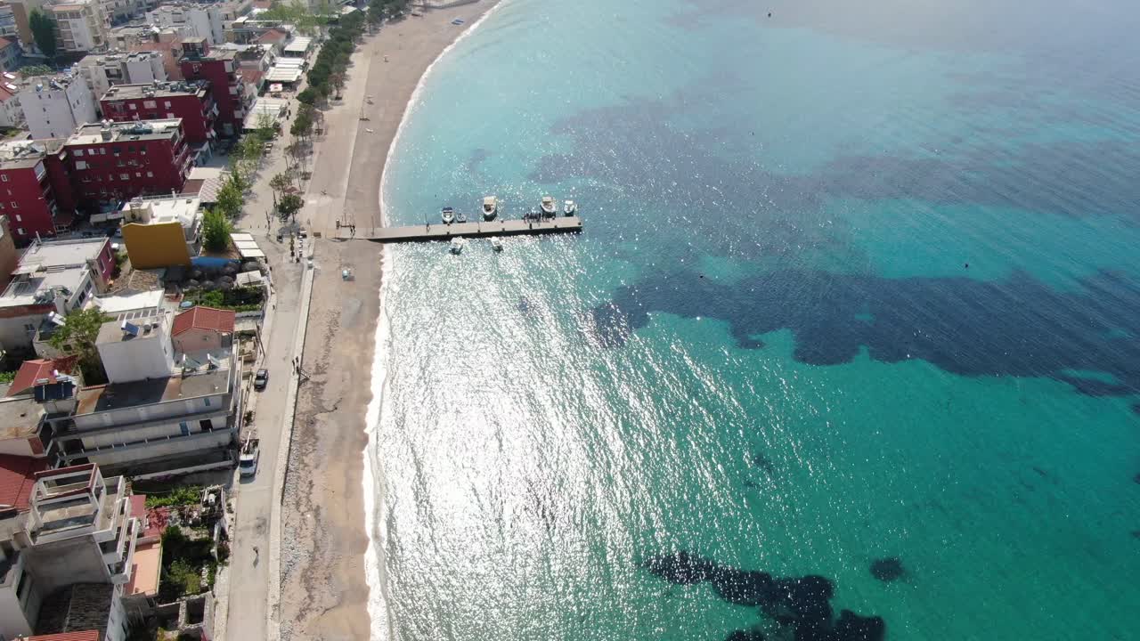 vista de avión no tripulado en albania volando sobre una playa con agua azul cristalina océano, edificios en el puerto y isla verde en un día soleado