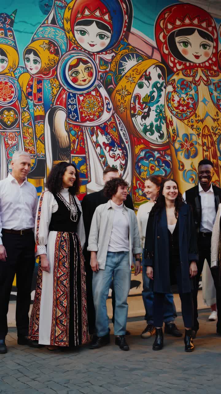 A diverse group stands in front of a vibrant mural featuring traditional dolls