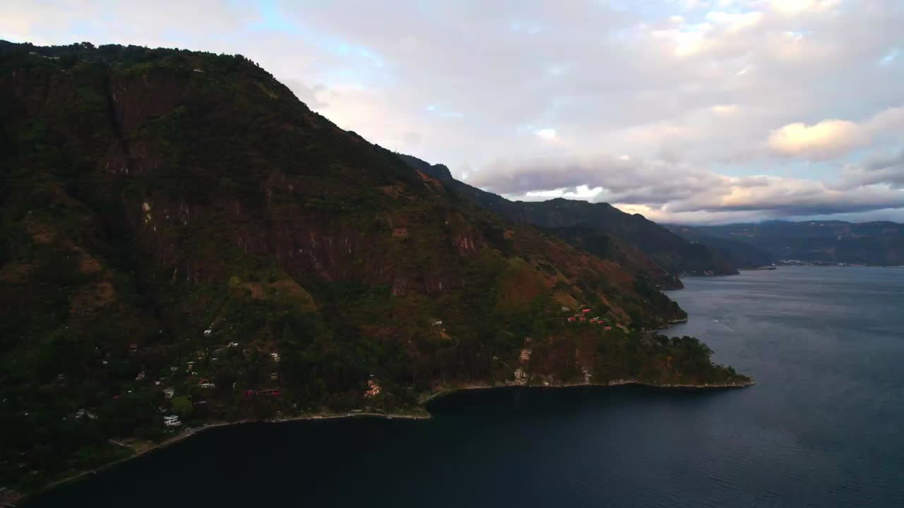 Ampia vista aerea del lago di Atitlán al crepuscolo con silhouette scure delle montagne, nuvole soffici e superficie dell'acqua riflettente