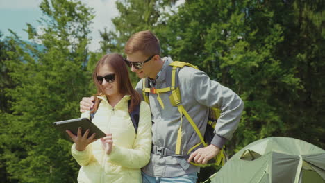 una pareja joven de turistas disfruta de una tableta en el puesto de camping cerca de la tecnología de la tienda de vacaciones