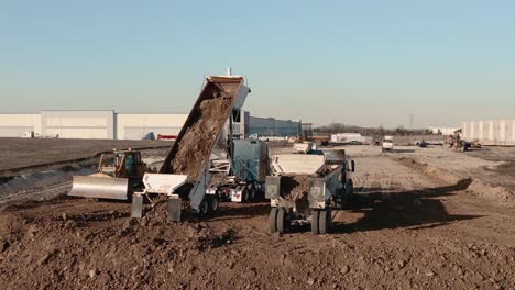 a dump truck full of dirt on a construction site drops its load