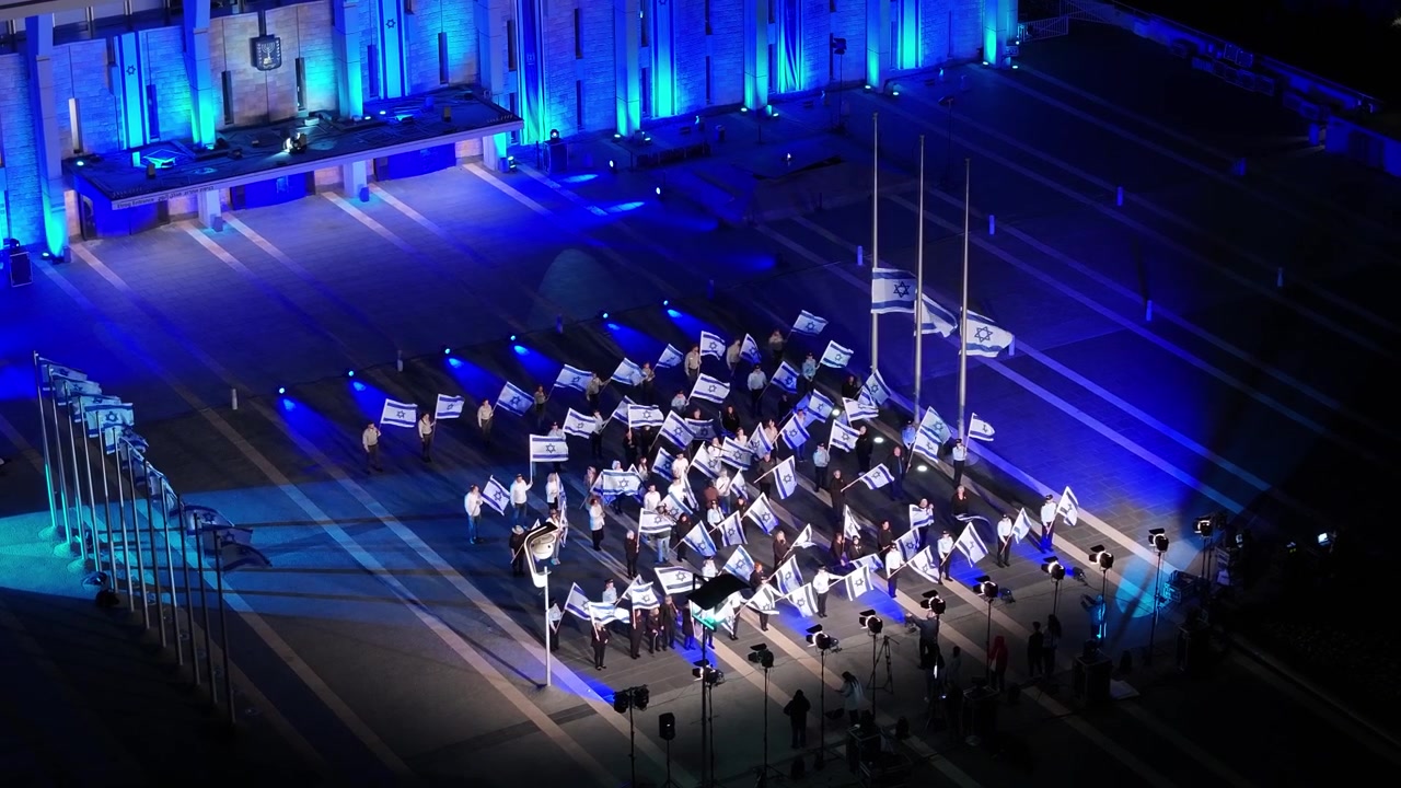 Un gruppo di persone che sventolano bandiere israeliane riunite in una piazza illuminata a giorno durante un evento notturno a Gerusalemme.