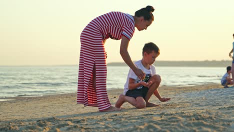 woman and a boy on the seacoast. mother in long dress is having good time with her son together on the sand beach during summer holidays.