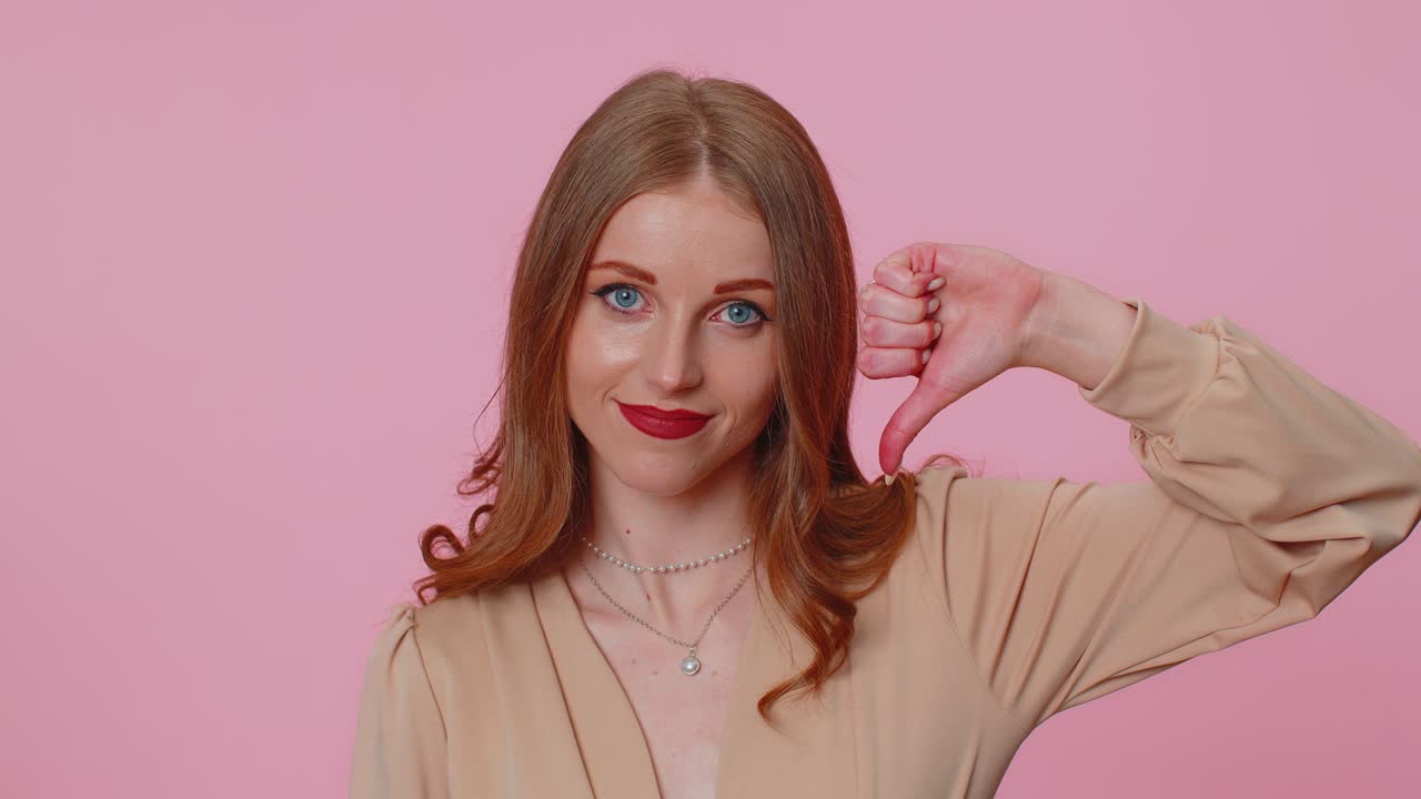 Upset girl in beige blouse showing thumbs down sign gesture disapproval dissatisfied dislike
