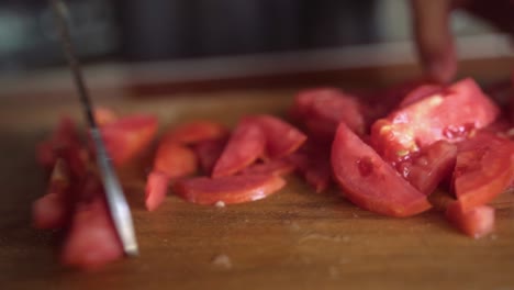 cutting tomato slices on wooden cutting board, female hand, close up