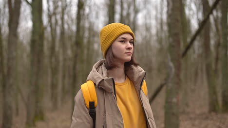 a young girl in a yellow woolen hat walks through the forest looking from side to side 1