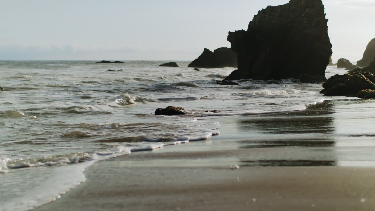 Ocean waves washing onto a sandy beach with large rock formations
