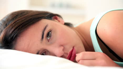 unhappy brunette lying in bed looking at camera