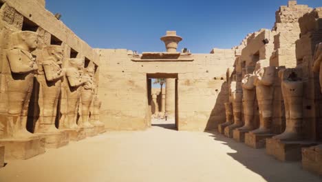an entry way into the kamak temple with tall statues lining each side on a sunny day in luxtor, egypt. static shot with a person in the distance to show the massive scale.