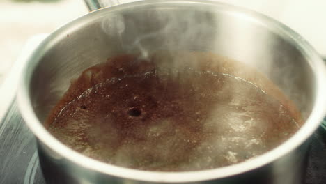 closeup hot chocolate boiling in metal bowl on stove.