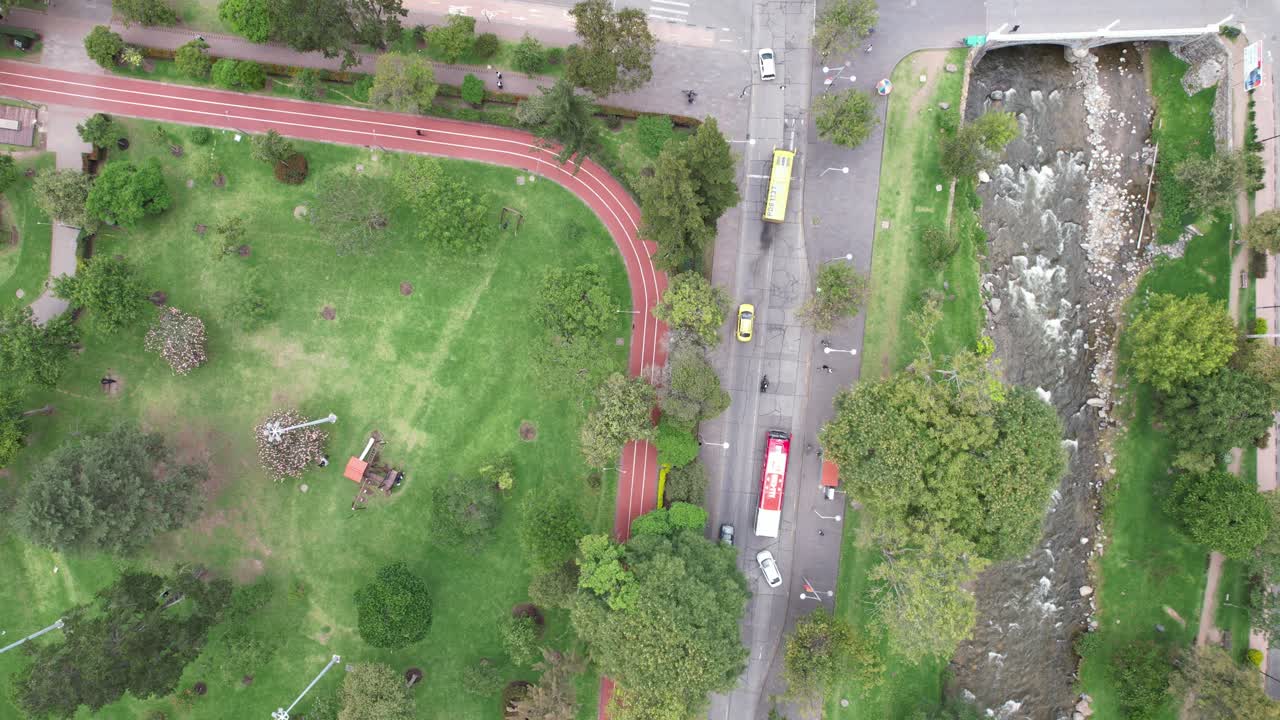 4K aerial drone shot over Parque de la Madre in Cuenca, Ecuador. Follows the red running track, capturing sports, green trees, playground, and people enjoying morning activities.