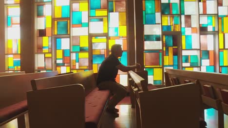 wide dolly shot of a young ethnic man praying inside of a church sanctuary