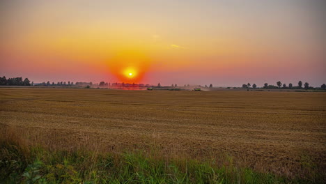 Cinematic-time-lapse-footage-of-farm-workers-driving-tractors-on-a-field-while-the-sun-is-setting-in-the-background,-Timelapse