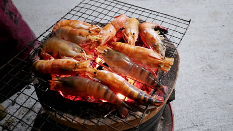 Grilling-big-prawns-on-fiery-red-coals-on-top-of-a-grill-in-a-food-stall-in-Bangkok,-Thailand