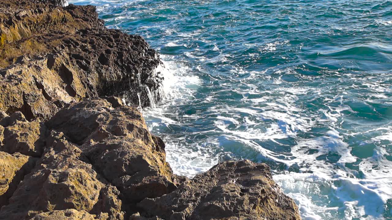 Slow motion footage of powerful turquoise ocean waves crashing against sharp rocky cliffs near Boca do Inferno in Cascais Portugal on a sunny day