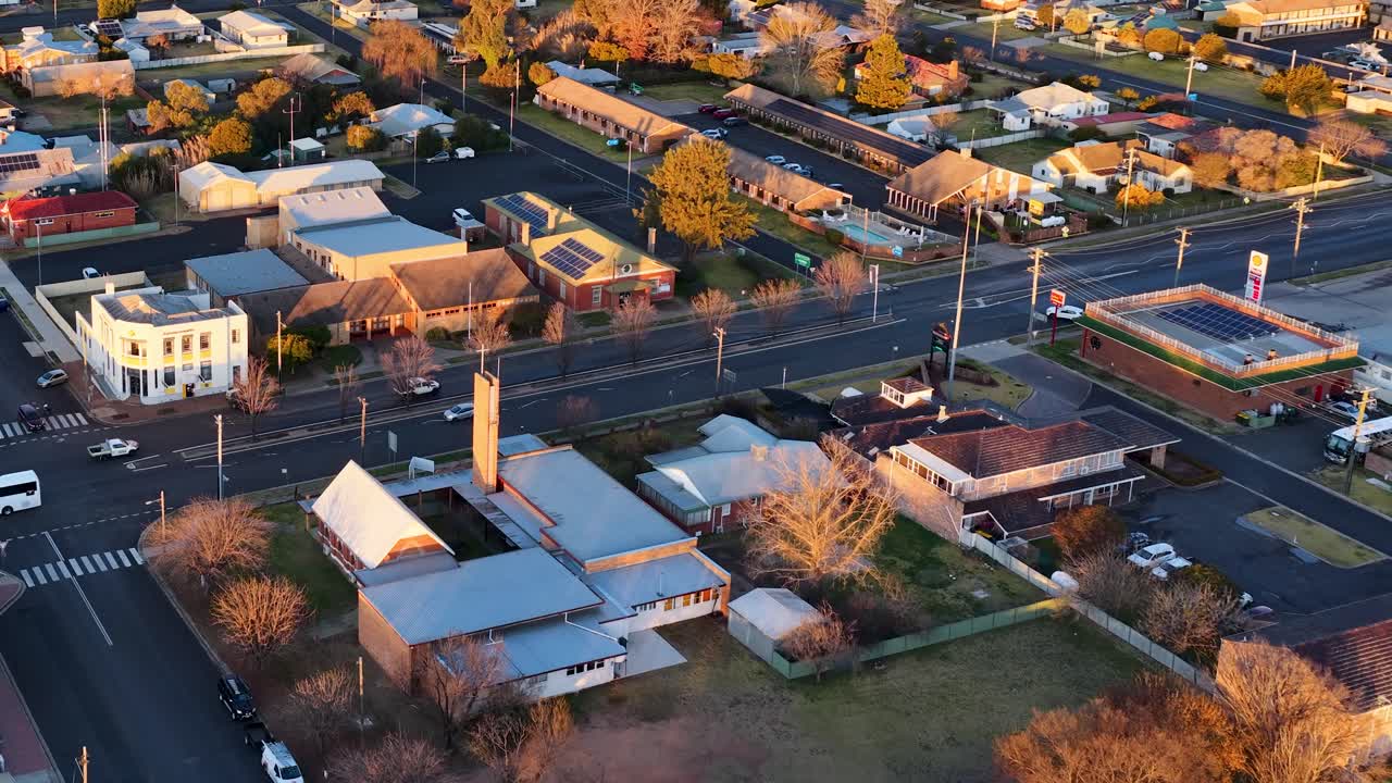 Drone footage captures a sweeping aerial view of Coonabarabran, New South Wales, during golden sunset light, highlighting streets, buildings, and residential areas
