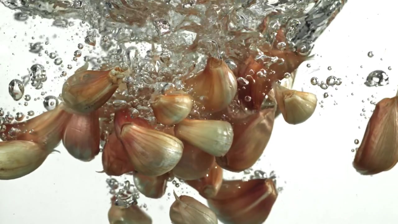 Fresh Garlic Cloves Splashing into Water with Bubbles
