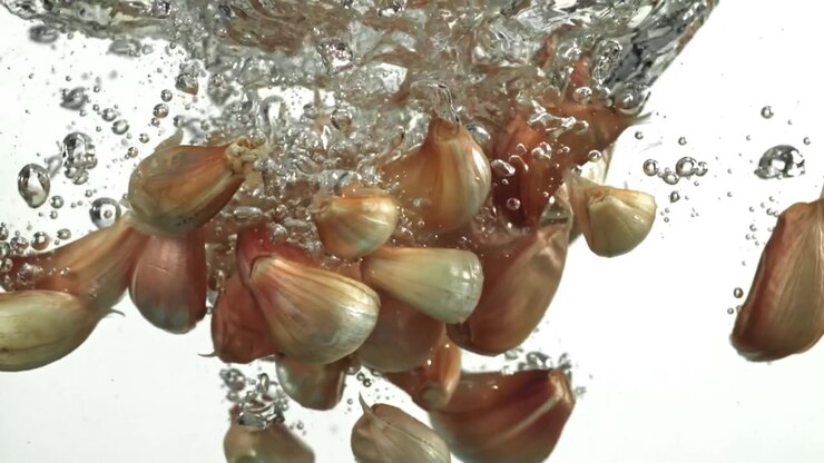 Fresh Garlic Cloves Splashing into Water with Bubbles