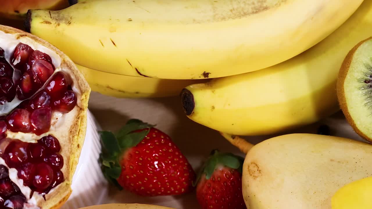 A colorful arrangement of bananas, kiwis, strawberries, mangoes, pomegranates, and pineapples on a bright background.