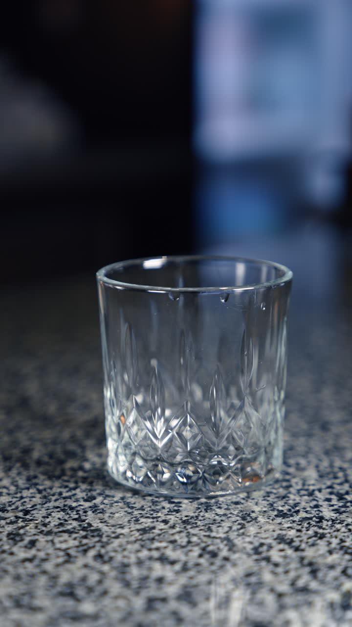 Ice cube is put into the little glass using metal tongs. Cocktail preparation in the bar or restaurant. Close up. Vertical video.