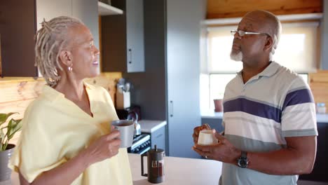 happy senior african american couple drinking coffee and talking in kitchen, slow motion