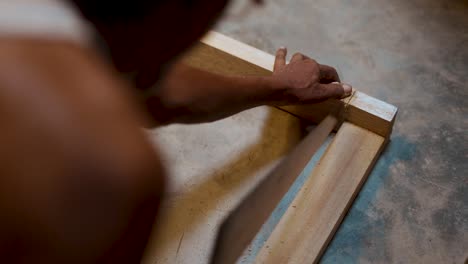 vista sobre el hombro de un carpintero cortando un trozo de madera con sierra transversal, carpintero usando una sierra transversal desde el ángulo superior, carpintero trabajando en su taller haciendo muebles