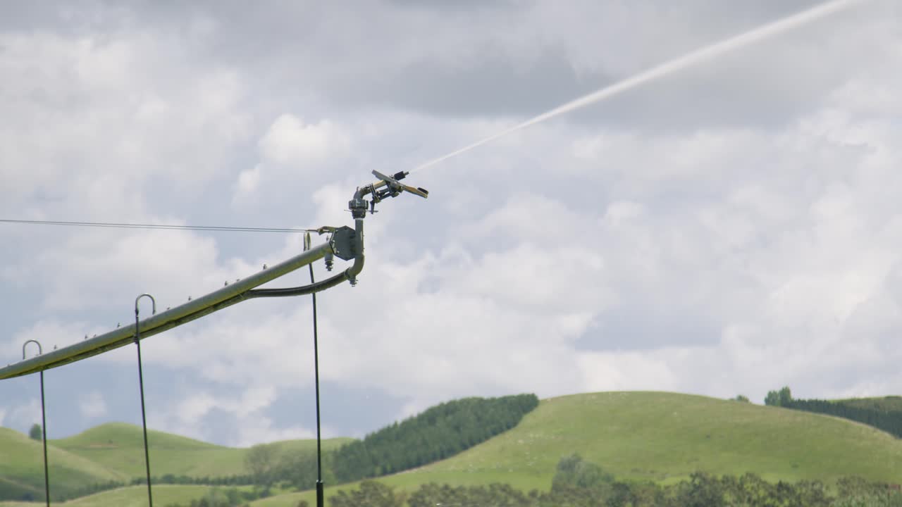 The sprinkler on the end of an irrigation truss spraying water with rolling green hills in the background