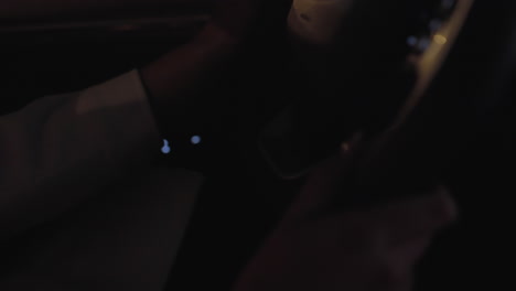 close up hand view of lady driving car at night, fingers gripping steering wheel with soft golden glow reflecting on her hand as vehicle moves through dimly lit surroundings