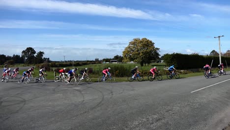 bunch of racing cyclists turn a corner at speed in countryside - north canterbury